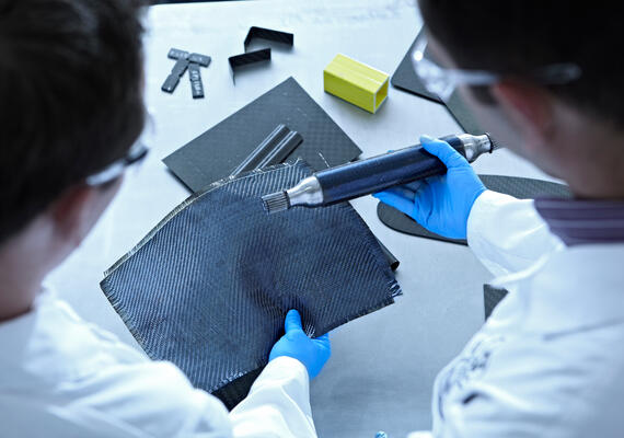 Two Researchers Inspect A Piece Of Woven Fibres With A Implement